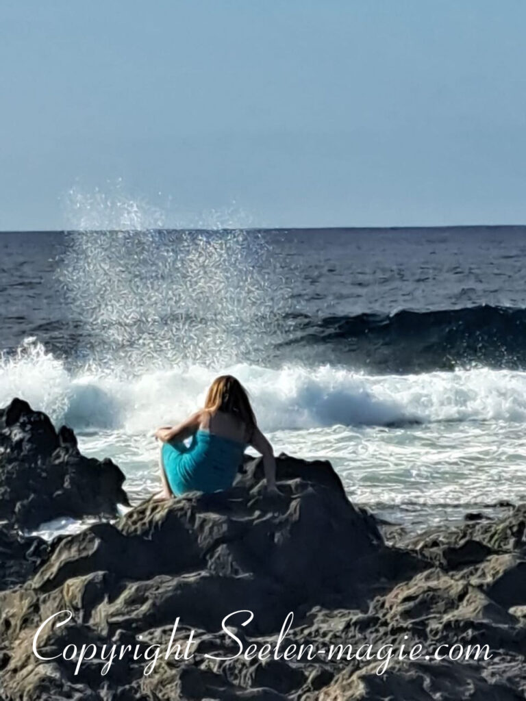 Jana Lübcke sitzt auf einem Vulkanstein am Strand von La Santa, Lanzarote